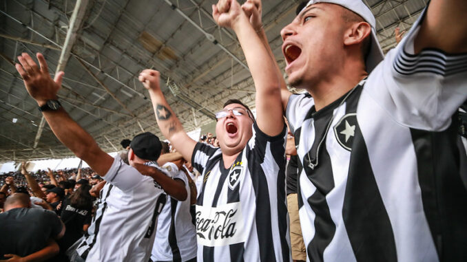 Um grupo de torcedores de futebol com camisas pretas e brancas torcendo.