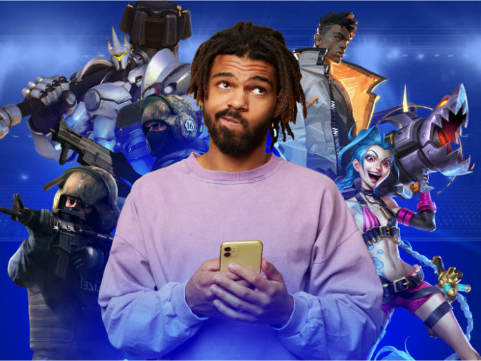 Um homem segurando um smartphone com uma colagem de personagens de videogame ao fundo.