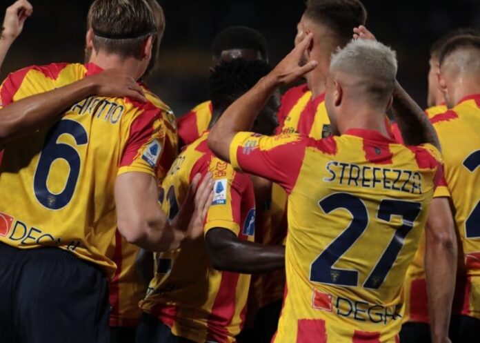 Jogadores de futebol com camisas amarelas e vermelhas se aconchegando antes de uma partida do Campeonato Italiano.