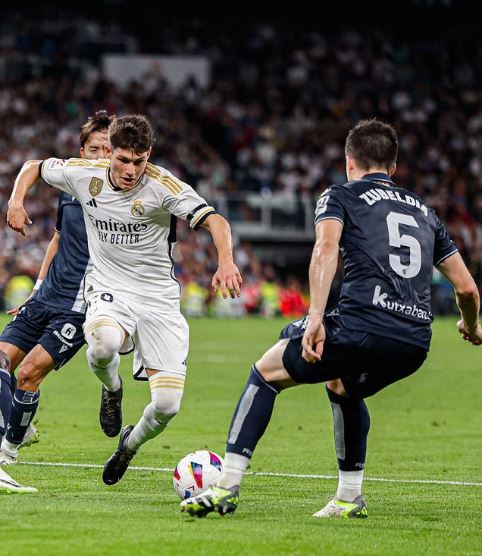 Dois jogadores de futebol de times adversários competem pela bola durante uma partida da Liga dos Campeões.