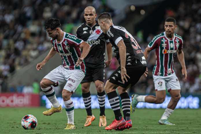 Dois jogadores de futebol do Fluminense FC disputam a bola contra um jogador do CR Vasco da Gama durante partida do Brasileirão 2023.